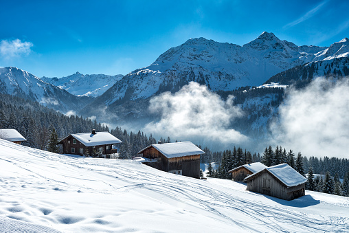 Beautiful winter landscape with ski lodges beside the ski slope and the forest in vorarlberg, austria. There is some fog in the background in front of the mountains of the alps.
