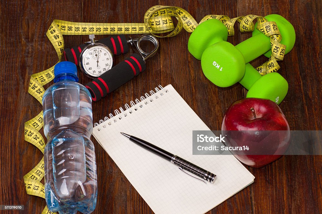 Workout and fitness dieting copy space diary. Healthy lifestyle concept. Workout and fitness dieting copy space diary. Healthy lifestyle concept. Apple, dumbbell, water, expander hand, stopwatch and measuring tape on rustic wooden table. Adult Stock Photo