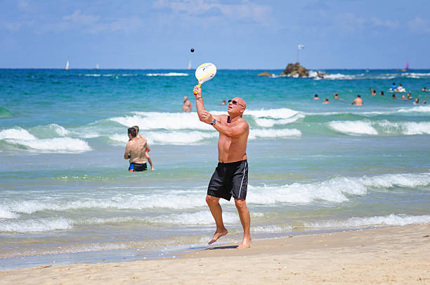 uomo suona matkot in spiaggia del mediterraneo - matkot foto e immagini stock