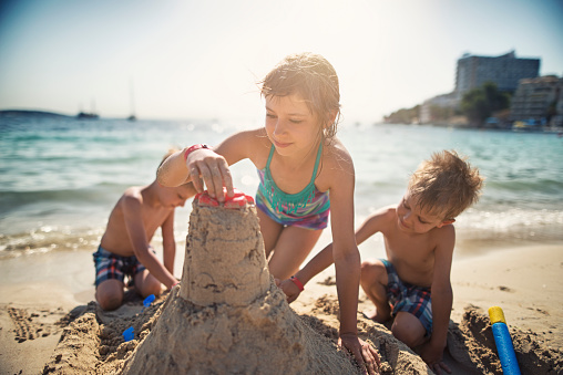 Brothers and sister having fun building a sandcastle on the beautiful majorcan beach beach. The girl is aged 9 and the boys are aged 4. Sunny summer day.