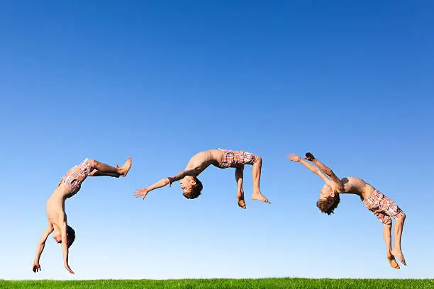 Young boy doing a backflip on a green meadow