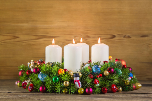 Colorful advent wreath with four white burning candles on wooden background.