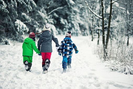 Three kids running in cold winter forest. The little girl is aged 10 and her brothers are aged 6. Back view.