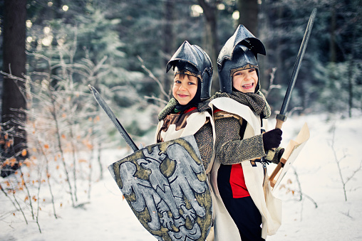 Brave little knights on a quest in a mystical frozen forest. Two little boys are standing back to back, shields up, swords in theirs hands. The horde of imaginary enemies are approaching on them but they are determined to fight them off.
