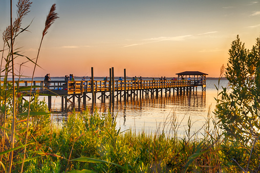 August 14, 2015 Fort Fisher Air Force Recreation Center, Kure Beach, North Carolina, USA: Tourists watch the sunset from the pier jutting out over the Cape Fear River.