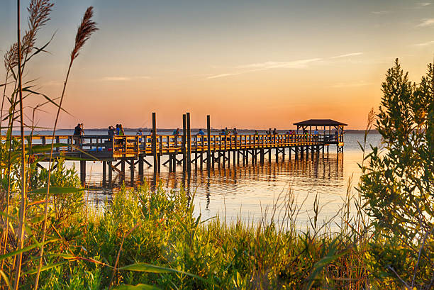 Cape Fear River August 14, 2015 Fort Fisher Air Force Recreation Center, Kure Beach, North Carolina, USA: Tourists watch the sunset from the pier jutting out over the Cape Fear River. cape fear stock pictures, royalty-free photos & images