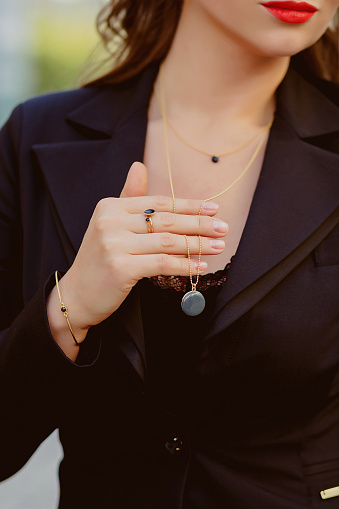 A girl holds a pendant close up. We can see part of his face, red lips.