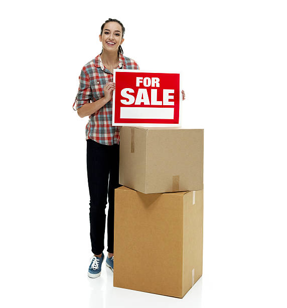 istock Smiling female holding for sale sign and box 511381720