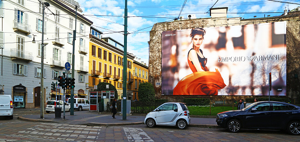 Milan, Italy - February 19, 2016: a giant billboard of Emporio Armani in central street. Some people and cars are visible in the picture.