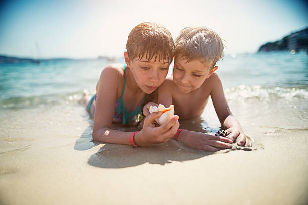 Young caucasian boy and girl jumping into waves. They are swimming and diving in clear turquoise colored sea.