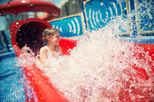 Little girl having fun sliding on water slide in water park. The girl is aged 9. Focus on the splash the girl is out of focus.