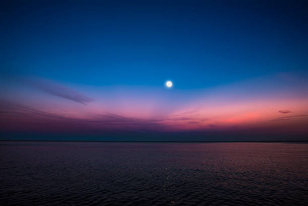 A wide angle capture of the moon, sky, and Lake Michigan at the fall of dusk.