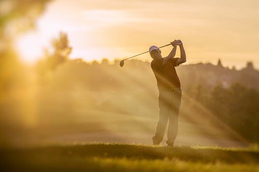 Mid adult golfer teeing of at sunset.