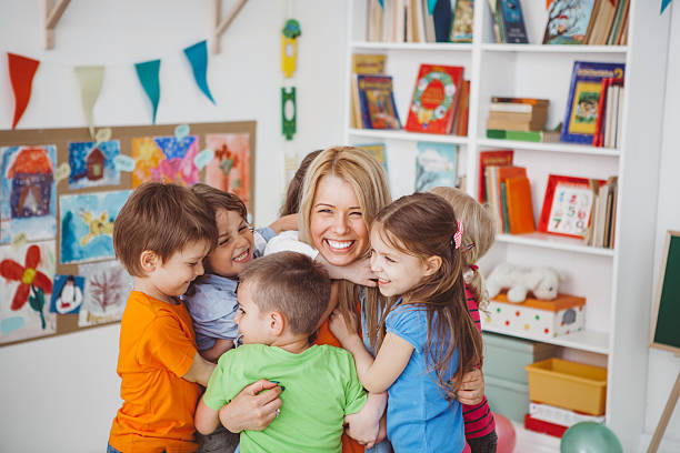 We love our teacher Kids in kindergarden playing with their teacher.They are hugging her to express their love. nursery stock pictures, royalty-free photos & images