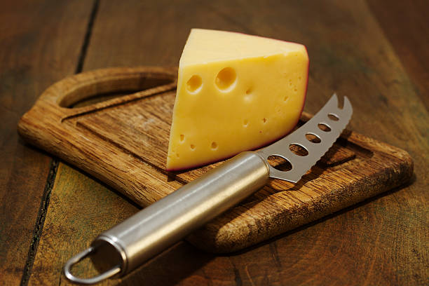 gouda cheese a piece of gouda cheese next to a knife, on a chopping board. gouda cheese stock pictures, royalty-free photos & images