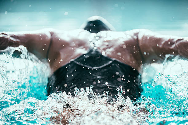 Butterfly stroke swimmer from back. Focus on water ripple