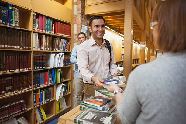 istock Mature female librarian handing a book to young man 511388855