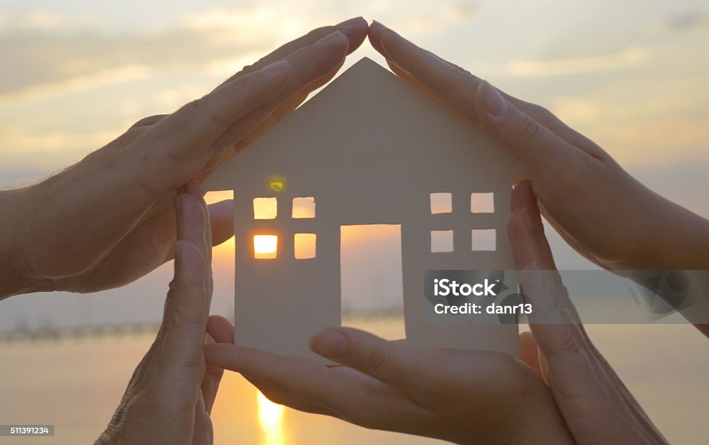 Hands on cut out house diagram Group of human palms on all sides of a cut out house diagram with setting sun coming through window over water Hope - Concept Stock Photo