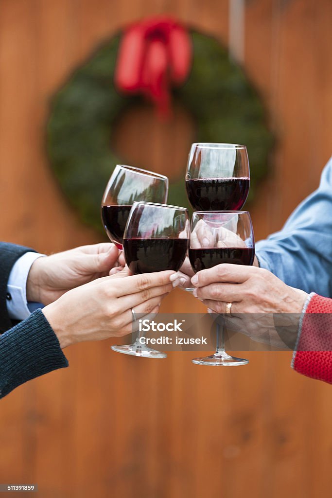 Christmast toast Four people toasting with red wine against doors decorated with christmast wreath. Close up of wine glasses. Adult Stock Photo