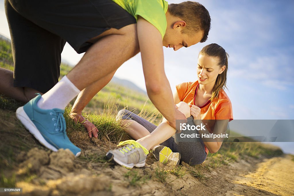 Female runner with injured knee Injury - sports woman with injured knee getting help from man touching her knee. Assistance Stock Photo