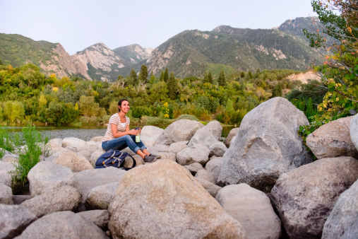 Female sitting on rocks by a lake in the mountains, holding a water bottle.