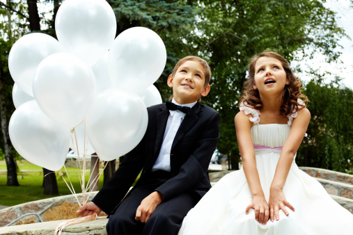 Portrait of children bride and groom with balloons sitting in park