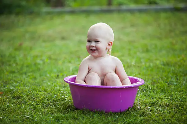 Happy toddler in a washbowl on the grass at the yard