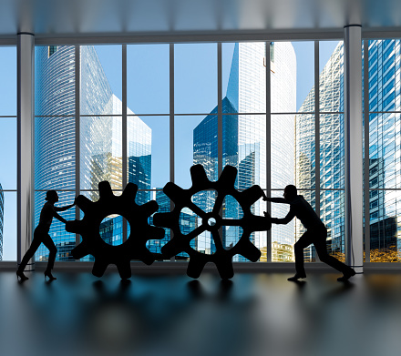 silhouettes of business partners moving gears inside an office in downtown business district
