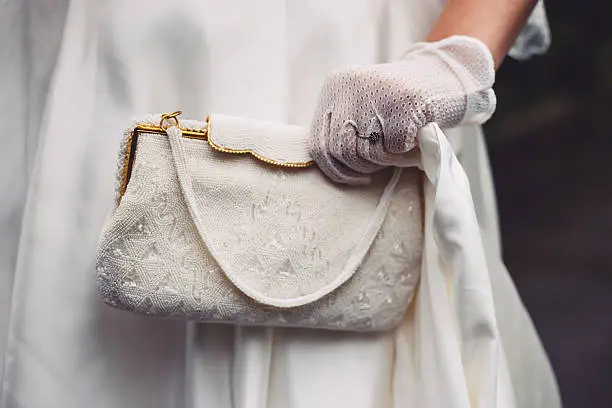 Bride holding white beaded purse bag. Pouch has gilded elements. Close-up.