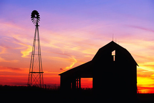 A beautiful sunset with a windmill and barn silhouetted against the evening sky in rural Indiana USA