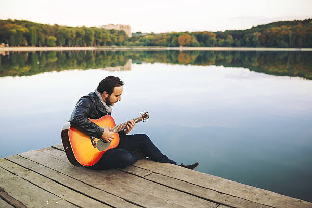 istock Young man playing on guitar at the lake 511477006