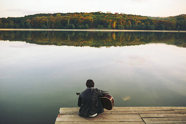 istock Young man playing on guitar at the lake 511477044