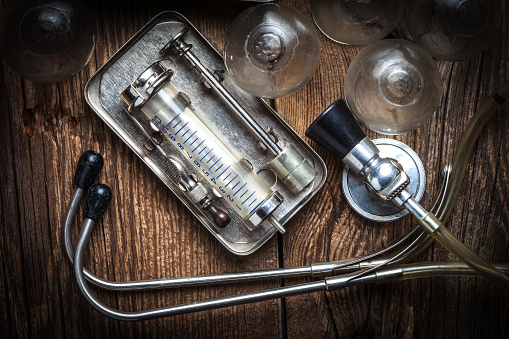 Retro syringe, stethoscope and medical cupping glass on a wooden table.