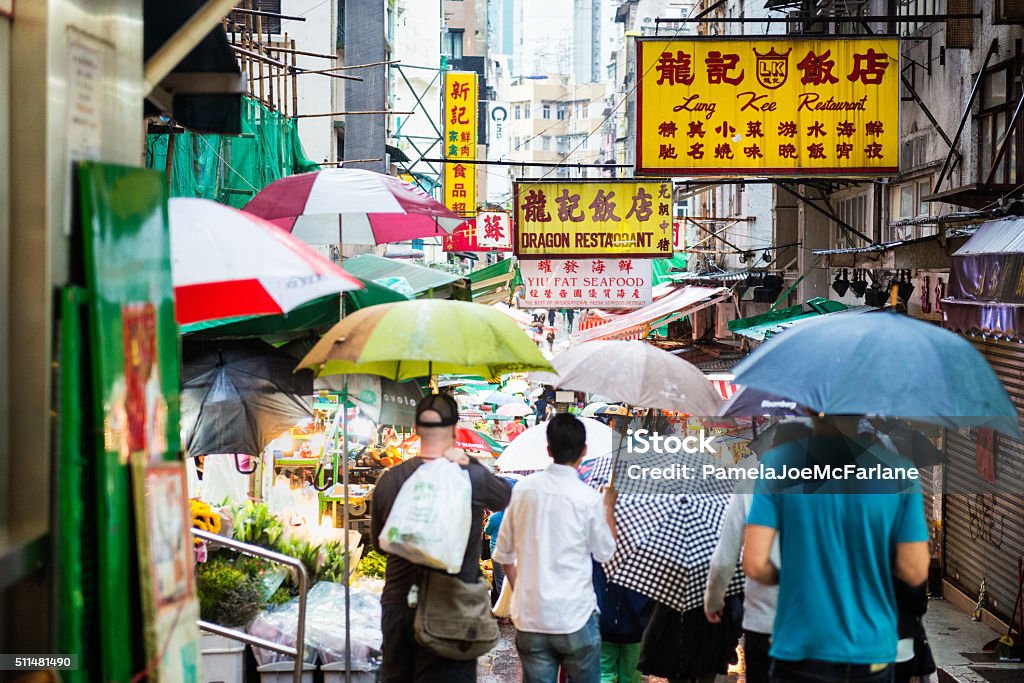 Crowd of Shoppers Walking Through Outdoor Market, Hong Kong, China Hong Kong iStockalypse.  Shoppers with umbrellas walk through a busy outdoor food market and restaurant area on a rainy day in Sheung Wan District, Hong Kong, China China - East Asia Stock Photo