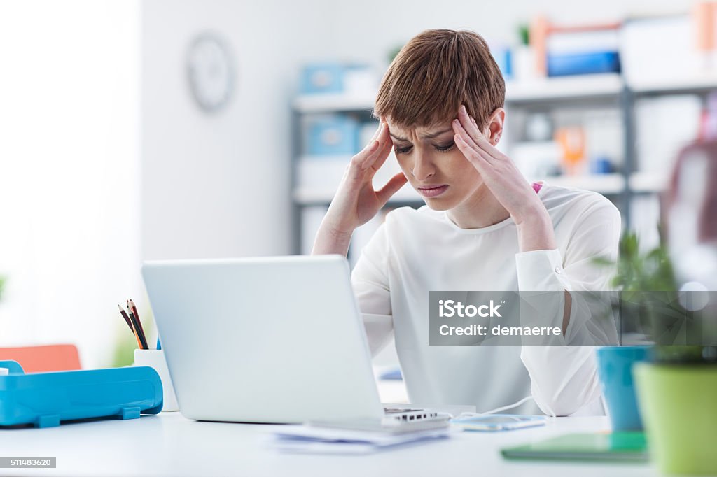 Stressed businesswoman at work Stressed young businesswoman working at office desk, she is having an headache and touching her head Adult Stock Photo
