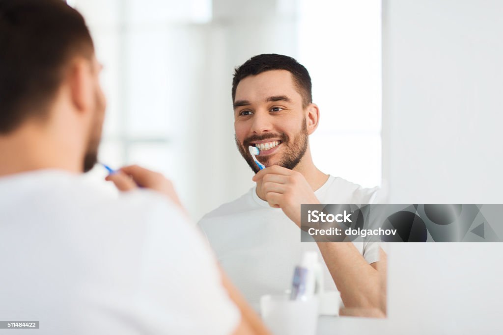 man with toothbrush cleaning teeth at bathroom health care, dental hygiene, people and beauty concept - smiling young man with toothbrush cleaning teeth and looking to mirror at home bathroom Brushing Stock Photo