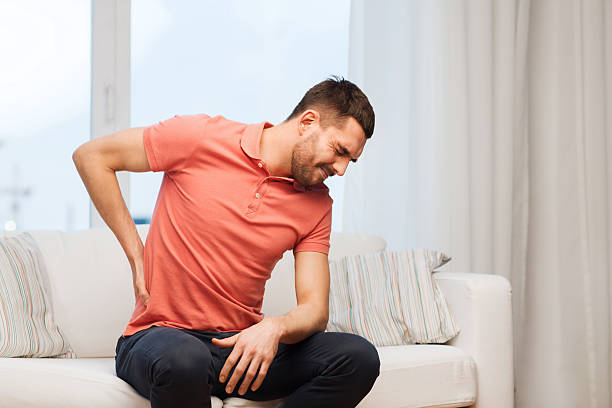 unhappy man suffering from backache at home people, healthcare and problem concept - unhappy man suffering from pain in back or reins at home back pain stock pictures, royalty-free photos & images
