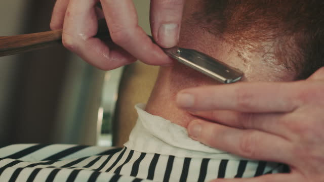 Barber shaving beard with razor