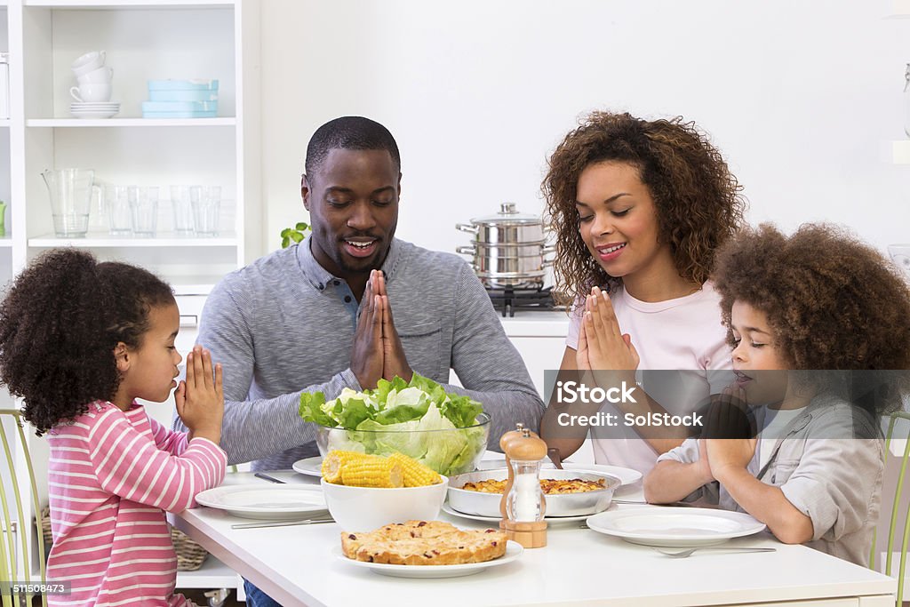 Family Sitting Down To A Meal Family put there hands together to say grace Family Stock Photo