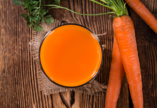 Healthy Carrot Juice (selective focus) on wooden background (close-up shot)