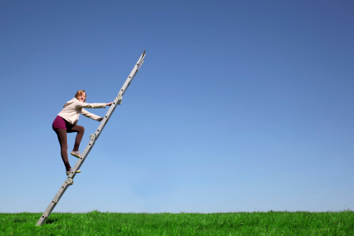 Young girl climbs a ladder on green meadow with blue sky