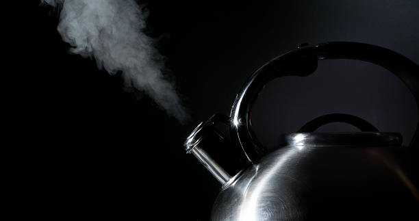 kettle whistling, boiling kettle, steam, on a black background stock photo
