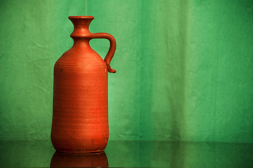 Pottery vase made of clay and painted in red against a green background.