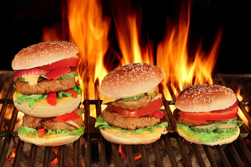 Three Different King Size Homemade Cheeseburgers In A Row On The Hot BBQ Grill With Flame Of Fire On The Black Background, Close Up, Front View