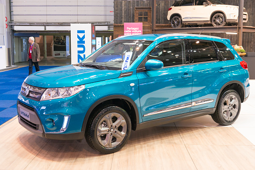 Brussels, Belgium - Januari 12, 2016: Blue Suzuki Vitara compact crossover SUV front view. The car is on display during the 2016 Brussels Motor Show. The car is displayed on a motor show stand, with lights reflecting off of the body. There are people looking around and other cars on display in the background.