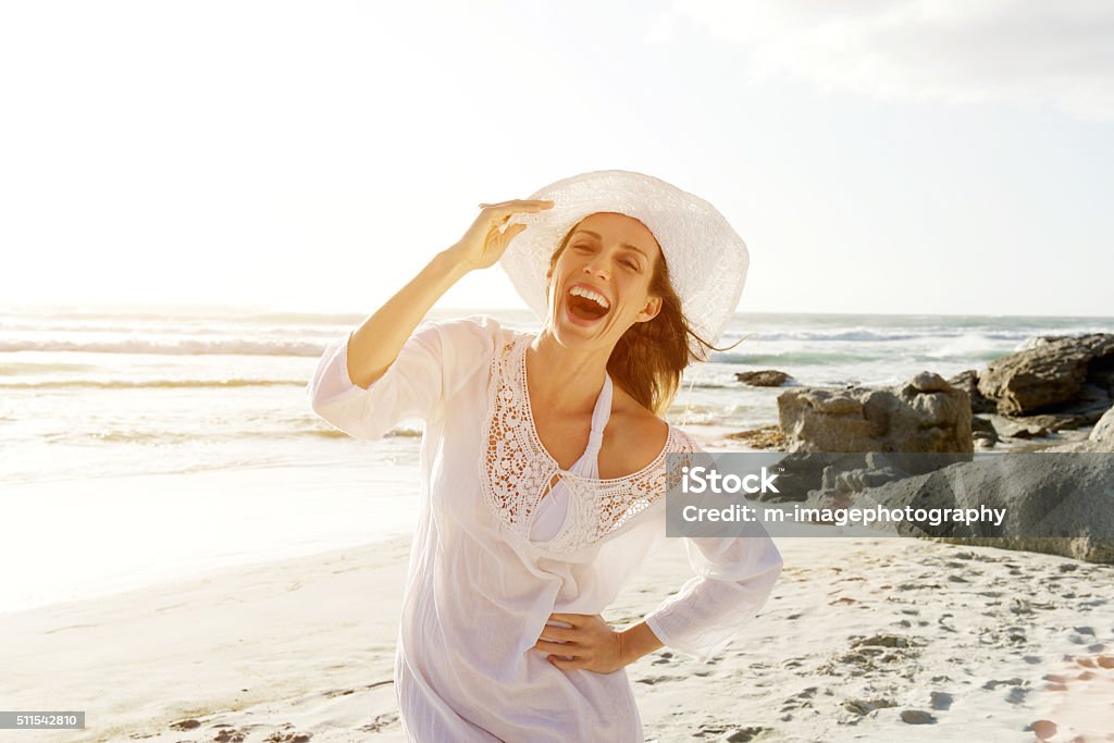 Entspannte Frau zu Fuß am Strand in der Sonne-Kleid und Mütze - Lizenzfrei Strand Stock-Foto