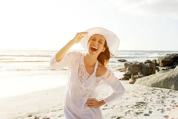 Photo of Carefree woman walking on beach with sun dress and hat