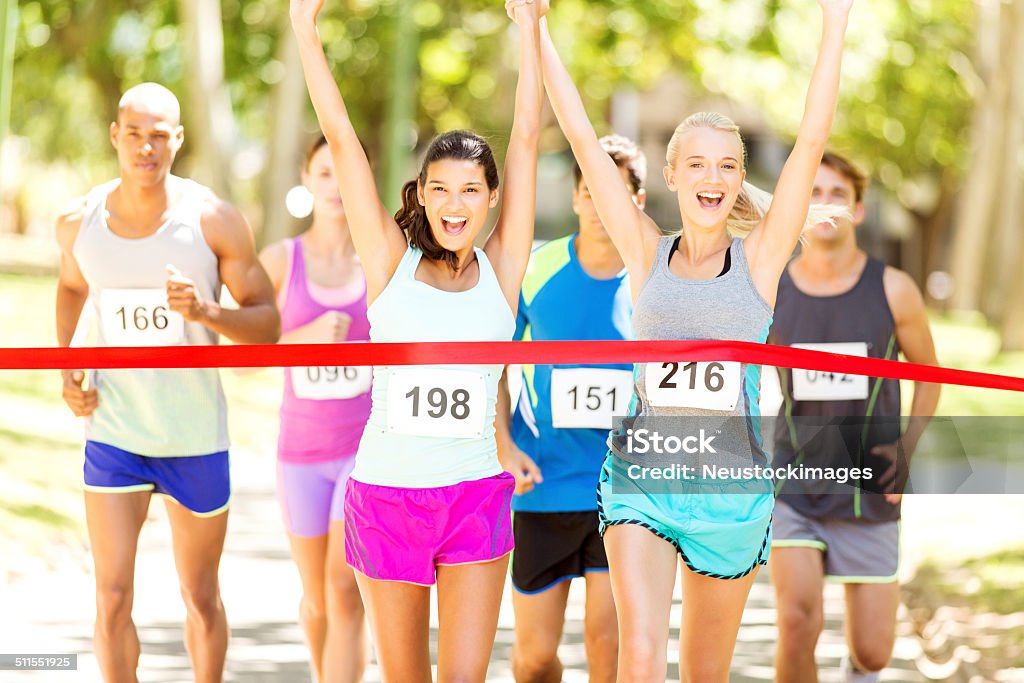 Female Marathon Runners Crossing Finishing Line In Park Portrait of excited female marathon runners crossing finishing line in park. Horizontal shot. 10000 Meter Stock Photo