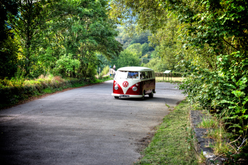 Dolgellau, United Kingdom - September 3, 2014: Old fashioned maroon and cream Volkswagen campervan being driven on Welsh country lane in the countryside of Gwyneddd. The driver and passenger are visble through the windshield