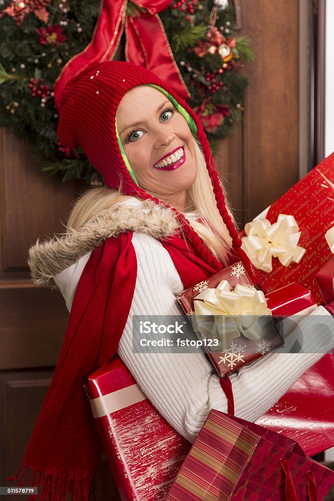 Christmas: Woman delivers holiday gifts or home from shopping day. Woman knocks on front door to deliver Christmas gifts to a neighbor or family member. Arrival Stock Photo